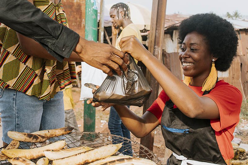 A trader serving roasted plantain to her client